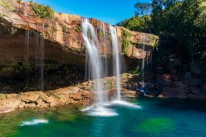 Capture of Krang Shuri Waterfall in Meghalaya, India with lush greenery and clear blue water.